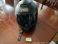 Front and side view of matte black Shoei full-face helmet showing the clear visor and Shoei logo.