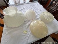 Five different large glass lamp shades on table, varying in textures and designs, approximately 14-16 inches in diameter.