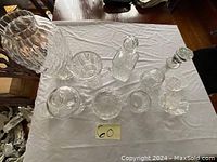 Top-down view of a large cut glass vase, four crystal decanters, and additional smaller glass and crystal items on a white cloth.