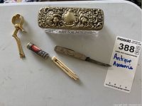 Five antique accessories shown including trinket box, dental floss container, pocket tool, ring glove holder, and nail tool on a white surface.