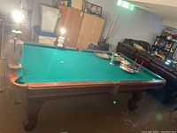 Full view of vintage slate pool table in basement with worn green felt surface and carved wooden legs.