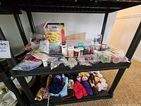 Shelf with assorted craft beads in containers and bags, wood ornaments, knitting needles, and wool yarn skeins below
