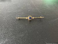 Front view of the 2.5 inch gold bar pin showing the blue central stone and side pearls.