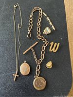 Full lot composition with all jewelry pieces arranged on a dark surface including chains, lockets, pins, and pendants.