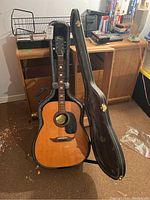 Front view of Thomas acoustic guitar in open black hardshell case with matching closed case beside it