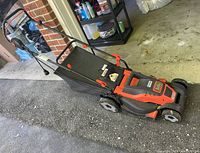 Full side and top view of the Black & Decker electric lawnmower showing grass catch bag, orange and black body, wheels, and handle with power cord.