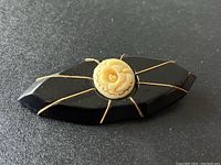 Full view of black mourning brooch with central rosette and gold wire accents showing entire piece.