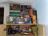 Image showing a cabinet top stacked with many boxed puzzles including I SPY 1000 piece, Puzzle 3D, and various colorful boxed puzzles mainly of 1000 piece counts.