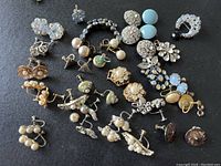 A large collection of vintage earrings, brooches, and buttons laid out on a black surface showing a varied assortment of rhinestone and pearl styles.