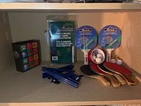 Four table tennis paddles with balls and foldable competition net on a shelf