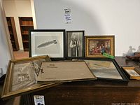 Multiple vintage framed artworks and two photo books placed on a surface, showing variety of subjects and frame sizes.