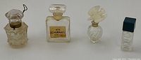 Four vintage mini perfume bottles including labeled Chanel N°5 square bottle, two glass stopper bottles, one rectangular with blue cap.