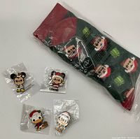 Lot contents including 4 packaged Disney Christmas enamel pins and one pair of Mickey Mouse Christmas socks in plastic packaging.