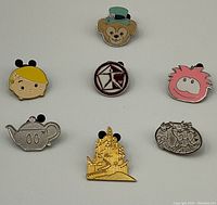 Front view of eight Disney enamel pins laid out on a white surface showing various colorful designs including characters and castle shape.