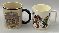 Photo of two vintage Disney mugs, one ceramic with black handle and vintage Mickey and Minnie Mouse "Home Cooking" design, the other white ceramic with square handle decorated with Mickey and Minnie Mouse in festive clothing.