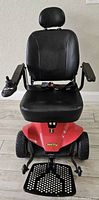 Front view of Jazzy Select Elite power wheelchair with black vinyl seat, red base, joystick on right armrest and foldable footplate