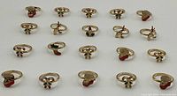 Top-down view of 18 vintage Christmas-themed rings arrayed in rows showing variety of holiday motifs including Santa hats, candy canes, stockings, reindeer, candle, and mistletoe.