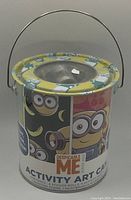 Photo of a cylindrical metal activity art can decorated with Minions graphics and Despicable Me branding, new condition with plastic lid and metal handle.