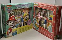 Photo of two activity sets: Paw Patrol Super Adventure Kit and Minions Super Activity Set, both in original packaging showing contents through clear windows.