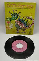 The vinyl record with pink label and colorful illustrated sleeve showing a whimsical dinosaur-like creature on yellow background.