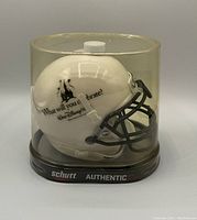 Side angled view of white mini football helmet with Walt Disney World themed decoration inside clear plastic protective case with black base.