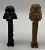 Two Star Wars vintage Pez dispensers, one of Darth Vader in black and one of Chewbacca in brown, both shown upright on white background.