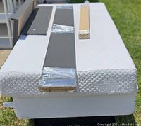 White twin mattress with floral embossing seen from the side, with frame parts wrapped in plastic on top