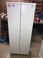 Front view of white laminate cabinet with two doors and handles, showing the overall cabinet appearance.