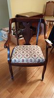 Front view of wood chair with upholstered floral cushion seat, curved armrests and casters
