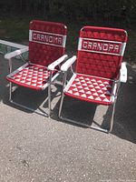 Front view of the two folding chairs side by side showing 'GRANDMA' and 'GRANDPA' text on backrests and the red and white woven patterns on seats and backs.
