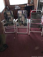 Three folding lawn chairs in a room, two with fabric cushions and one with metal slats.