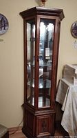 Full view of wood curio cabinet with glass door and mirrored back, showing multiple glass shelves inside.
