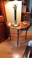 Full view of the wood demilune table with a green and gold lamp, cordless phone, and other small items on top, showing the size and style.