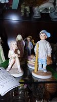 Porcelain figurines displayed on a shelf, showing detailed child figures with varying poses and accessories.