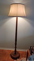 Full view of vintage wood floor lamp lit to show shade shape and lamp height relative to wall and floor.