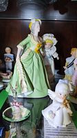 Side profile of Marie Antoinette porcelain figurine in green gown with surrounding porcelain dolls and figurines