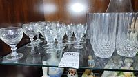 Shelf displaying small stemmed aperitif glasses, small crystal tumblers with cut designs, and two tall crystal tumblers with diamond-cut pattern.