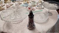Overview of glass serving dishes including cake plate, bowl, compote dish, and floral patterned sugar shaker on a white tablecloth.