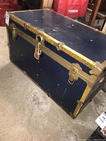 Cedar lined trunk closed, showing dark blue exterior with brass hardware, a lock with key, and scuff marks.