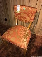 Front view of vintage wooden chair with orange-gold floral upholstery on seat and backrest.