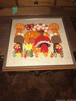 Frontal view of framed needlework showing the colorful mushroom and butterfly design.