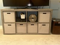 Front view of the 8-cube organizer with fabric storage bins, a TV stand placed on top, and various items inside compartments.