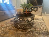 Full view of the silver-toned round coffee table showing the hammered metal surface, crisscross metal band base, and table height in living room setting.