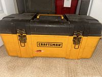 Front view of large yellow and black plastic Craftsman toolbox with metal latches and yellow handle showing Craftsman logo and wear on sticker.