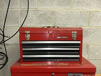 Red Craftsman tool box with two pull-out drawers and top lid closed, shown against concrete wall.