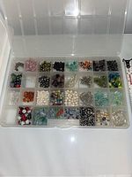 Overview of clear compartment box containing assorted beads and jewelry making supplies in multiple sections.