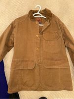 Full front view of the brown barn coat showing front button closure, corduroy collar and cuffs, and front flap pockets.