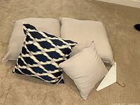 Full view of four pillows stacked, showing two taupe euro shams, matching smaller taupe throw pillow, and navy-cream decorative pillow
