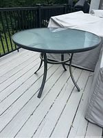 Full view of round frosted glass top outdoor table with black metal frame and four legs.
