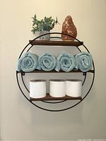Front view of round wall shelf with towels, toilet paper, plant, and salt lamp.